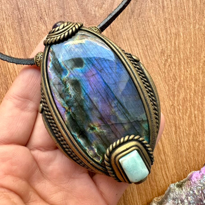 Hnamdade crystal and gemstone pendant necklace held by a hand on a wooden surface