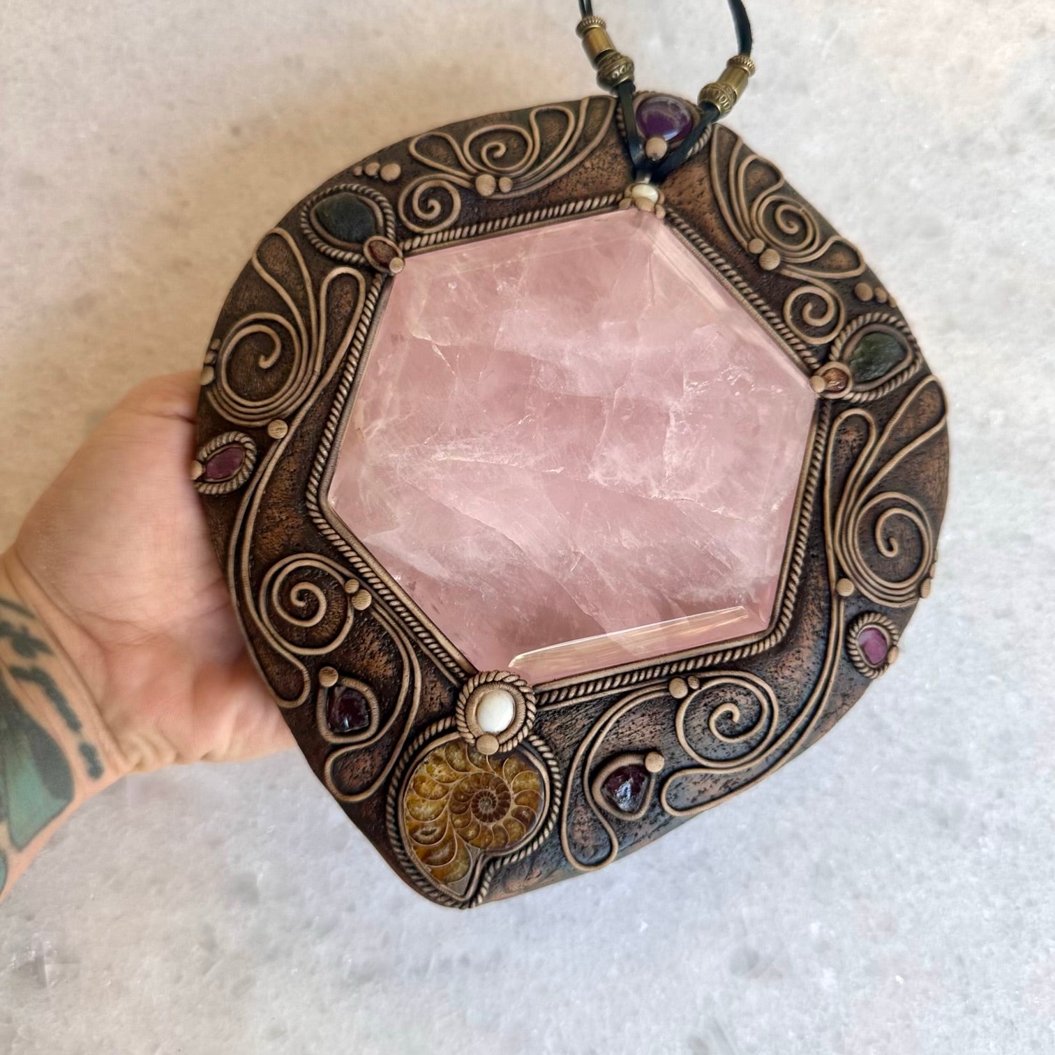 Decorative pendant with pink stone and bronze frame held by a hand on a light background