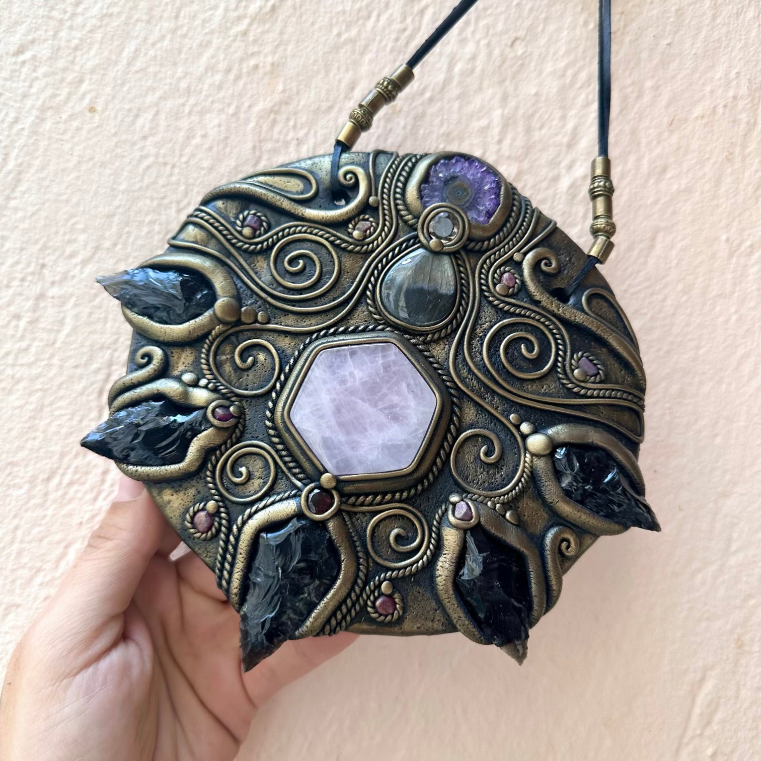 Decorative crystal wall art with intricate designs and gemstones held by a hand against a light background