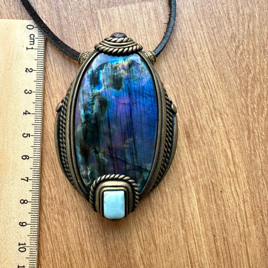 Necklace with a large, multicolored stone pendant on a wooden surface next to a ruler.