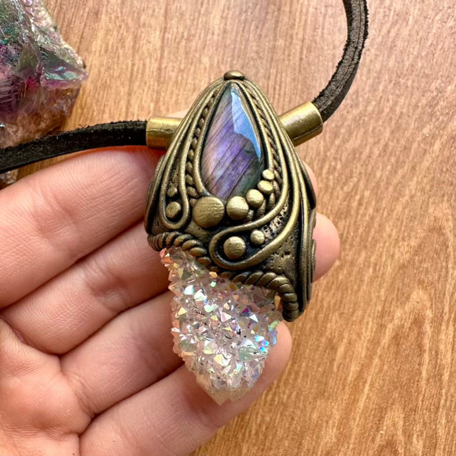 Necklace with ornate labradorite and angel aura spirit quartz pendant held by a hand on a wooden surface