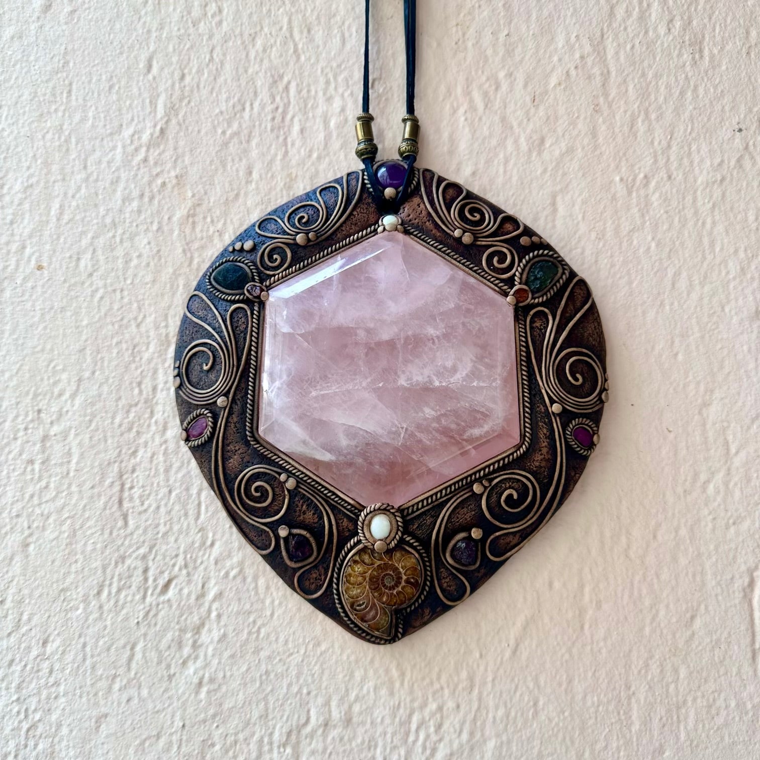 Decorative wall hanging with rose quartz stone and intricate metalwork on a white wall.