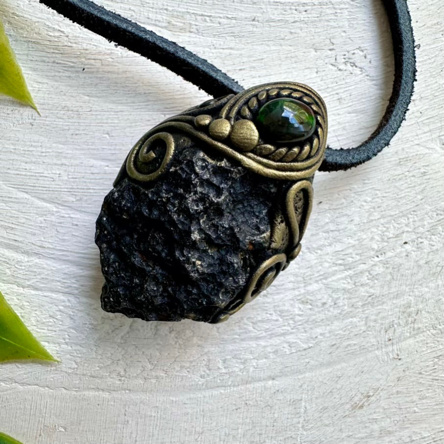 The Black Tektite and Black Ethiopian Opal Pendant Necklace is a handmade piece of unisex spiritual jewelry crafted with durable clay and an adjustable leather cord.