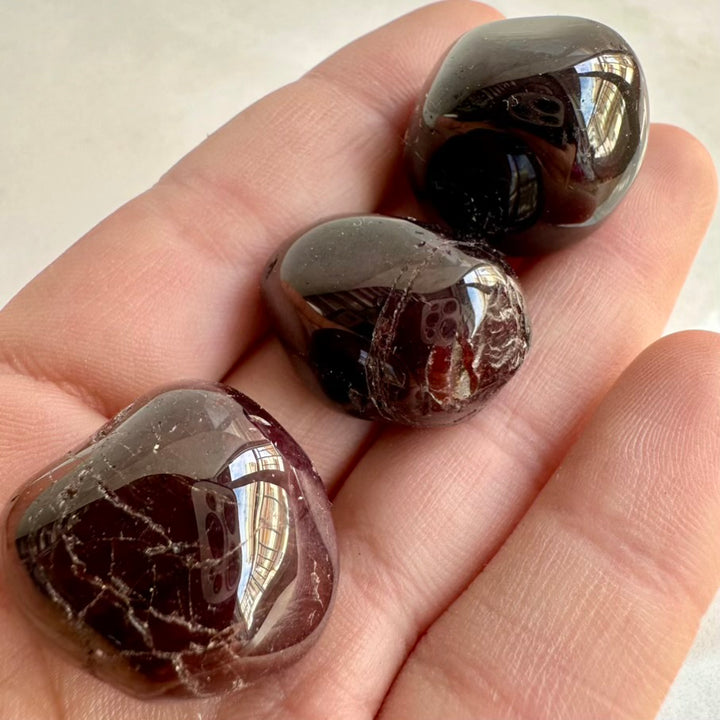 Three polished garnet gemstones held in a hand against a neutral background