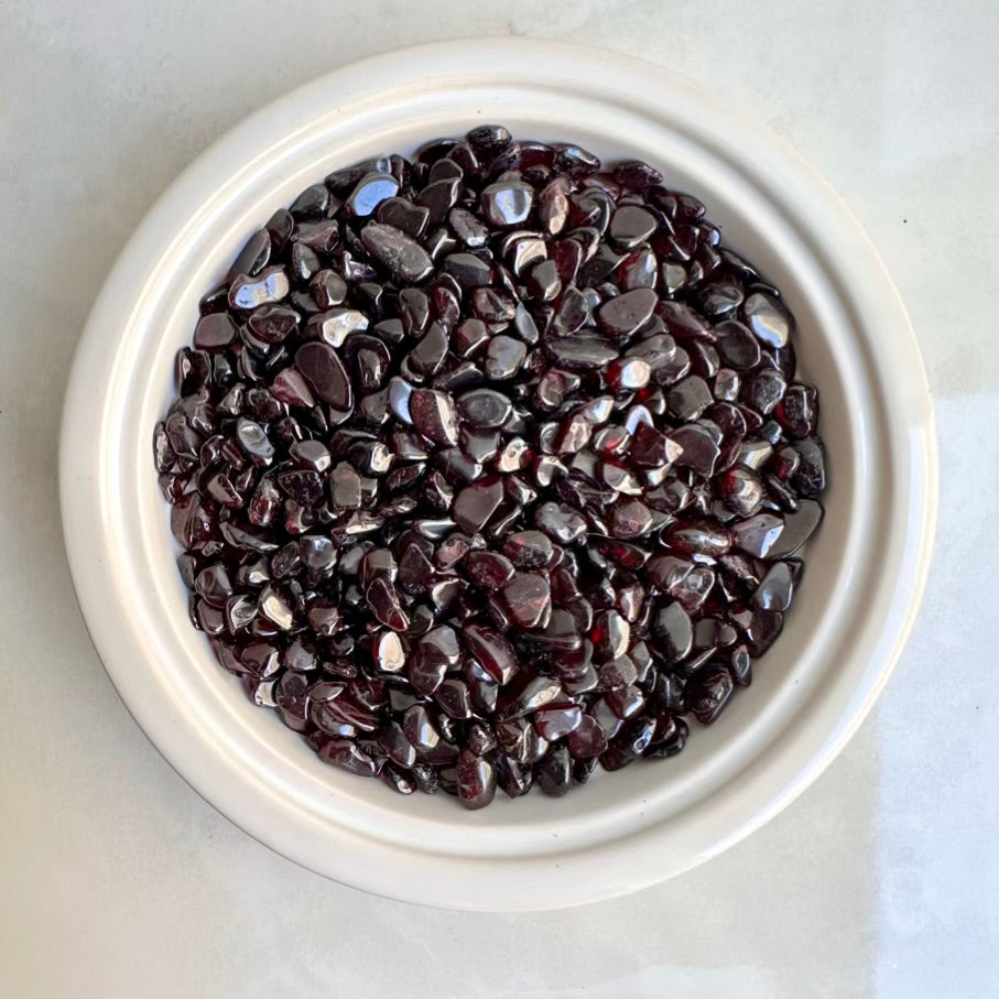 White bowl filled with red garnet stones on a light gray background