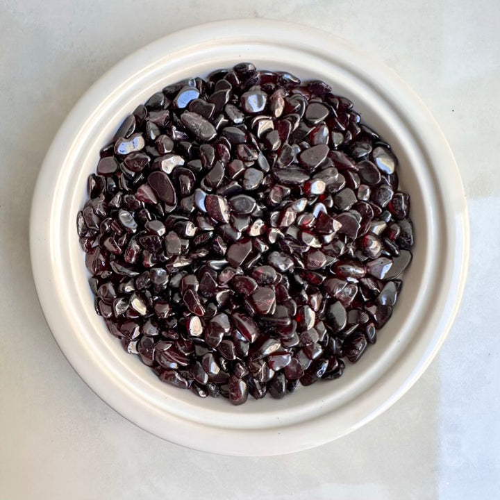 White bowl filled with red garnet stones on a light gray background