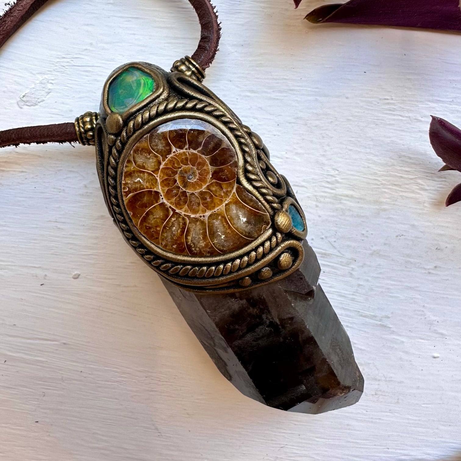 Ammonite fossil pendant on a crystal base with a brown cord against a white background