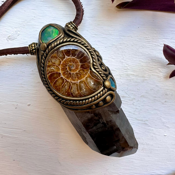Ammonite fossil pendant on a crystal base with a brown cord against a white background