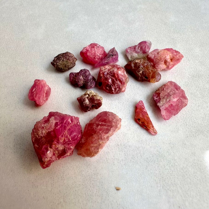 Raw pink and red spinel gemstones on a light gray surface
