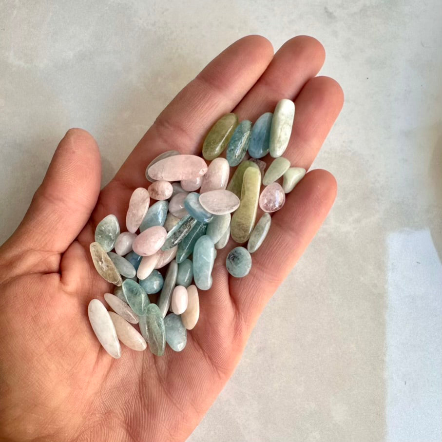 Hand holding a small collection of multicolored beryl stones against a neutral background