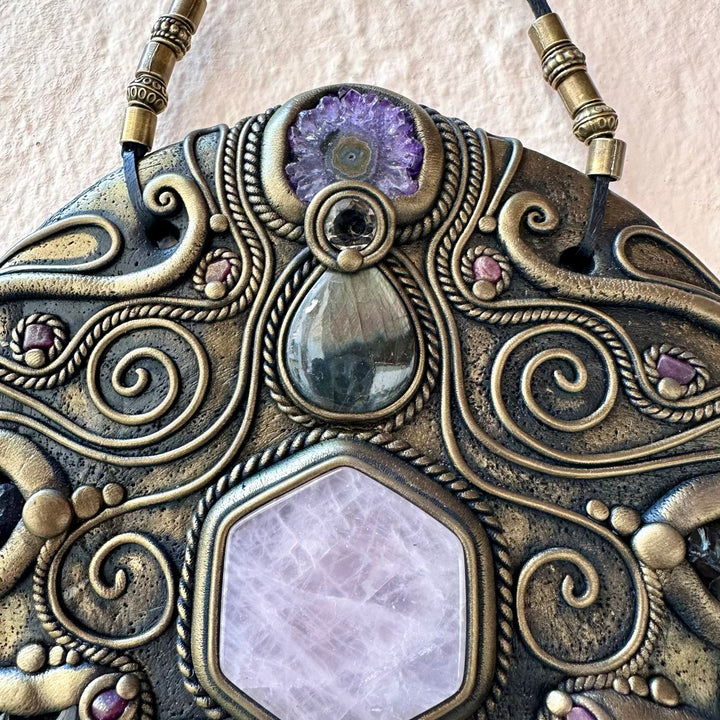 Decorative wall art piece with purple gemstones and intricate patterns on a textured beige background