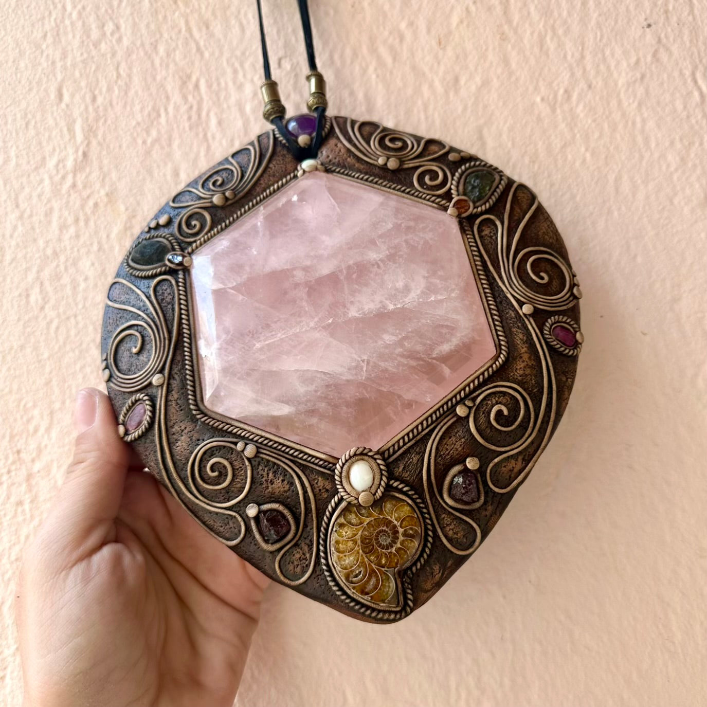 Decorative crystal pendant with rose quartz stone held by a hand against a plain background