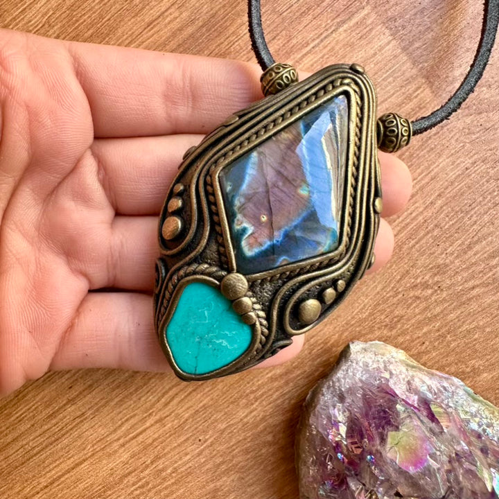 Decorative pendant with turquoise stone and labradorite held by a hand on a wooden surface