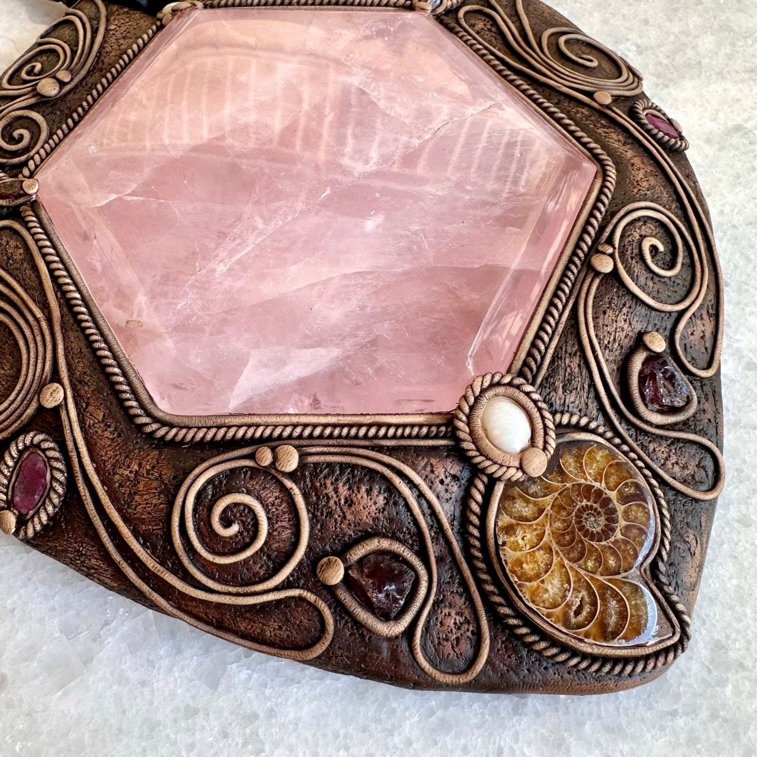 Decorative stone with pink crystal and ornate bronze frame on a white background
