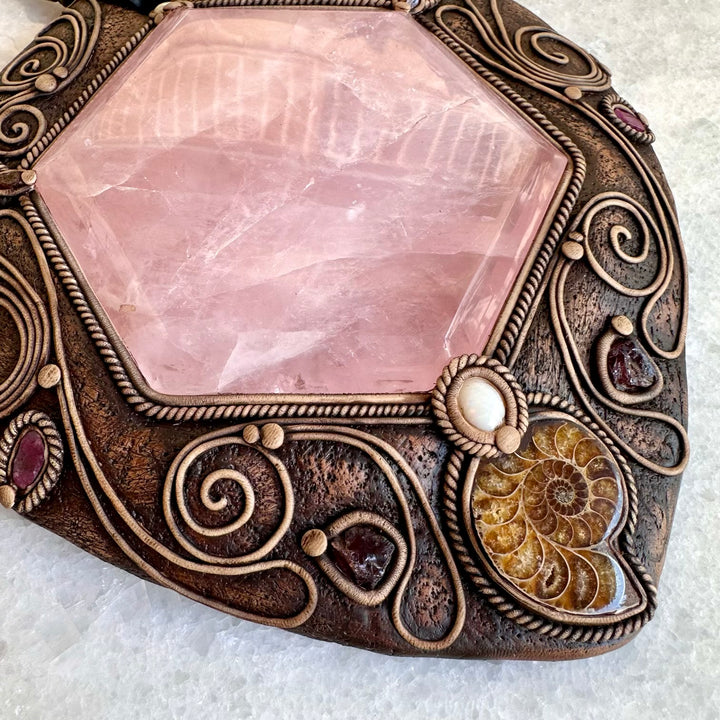 Decorative stone with pink crystal and ornate bronze frame on a white background