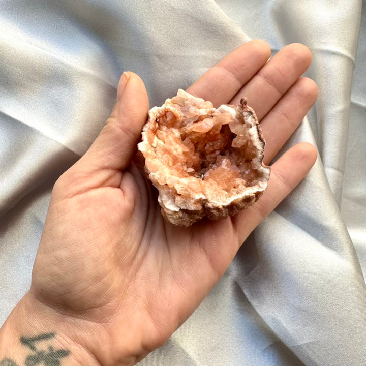 Hand holding a pink crystal geode against a light fabric background