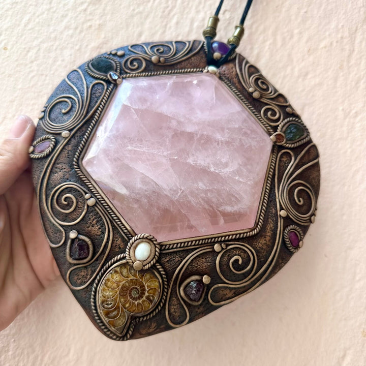 Decorative pendant with pink stone and intricate metalwork on a beige background