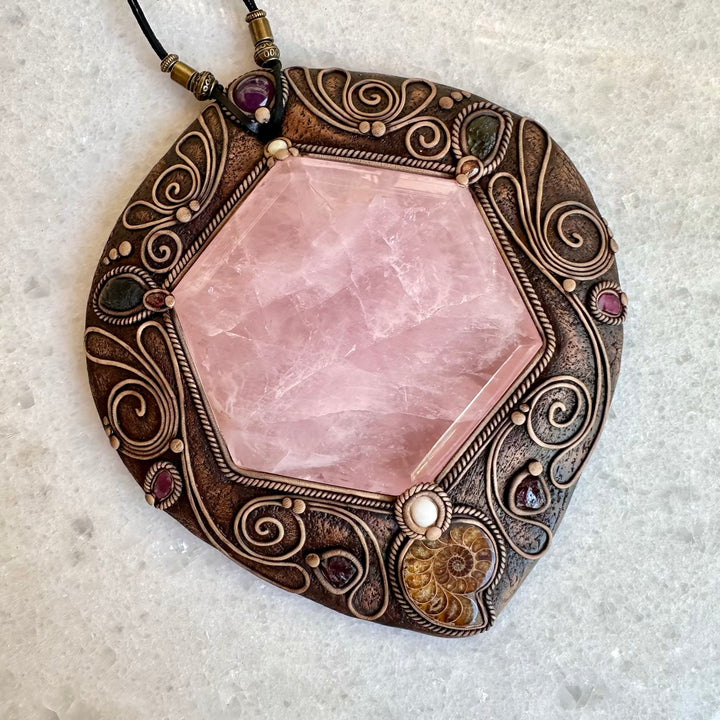 Decorative pendant with pink stone and intricate metalwork on a light gray background