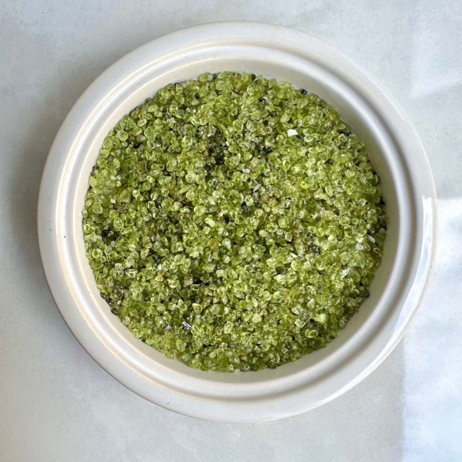 Small polished Peridot chips lot in a white bowl on a light gray background