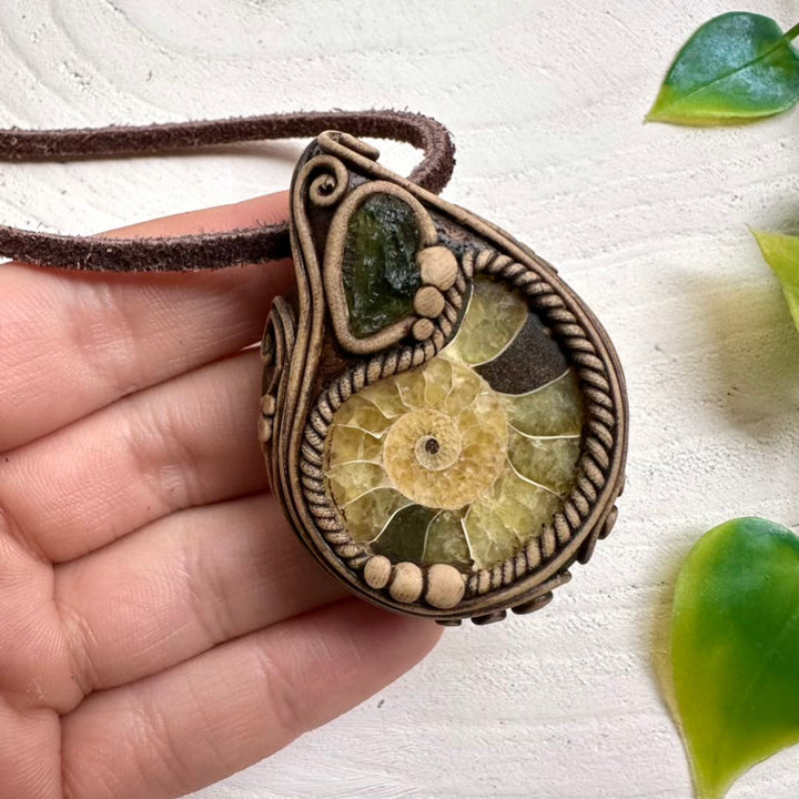 Hand holding a Ammonite and Moldavite crystal Necklace on a light background.