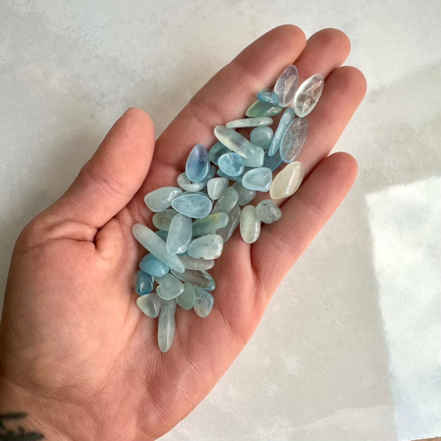 Hand holding a collection of small, transparent blue aquamarine stones against a white background