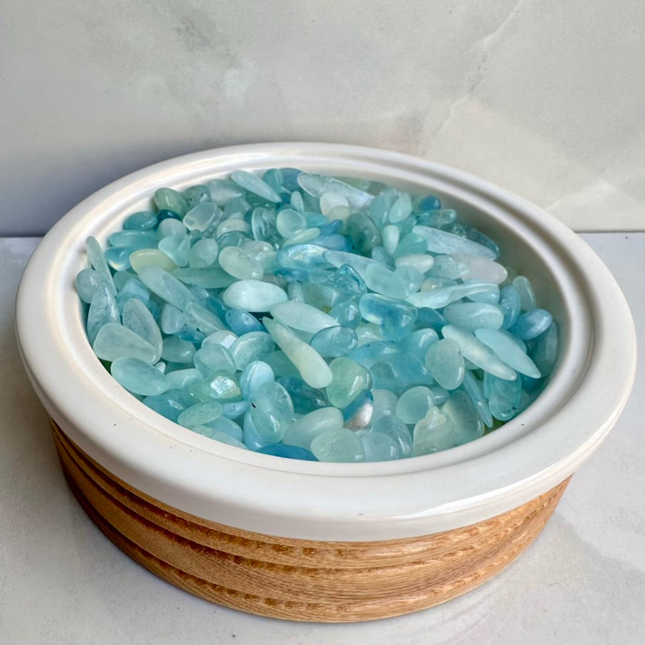Bowl filled with natural light blue aquamarine crystals on a white background
