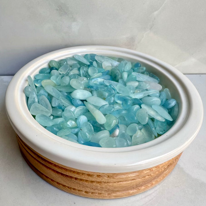 Bowl filled with natural light blue aquamarine crystals on a white background