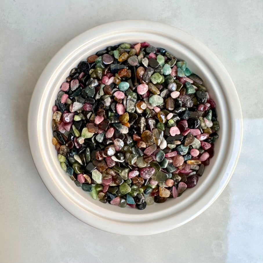 Assorted multicolored tourmaline stones in a white bowl on a light gray background