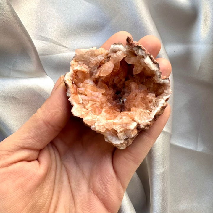 Hand holding a pink amethyst crystal rock against a silver fabric background