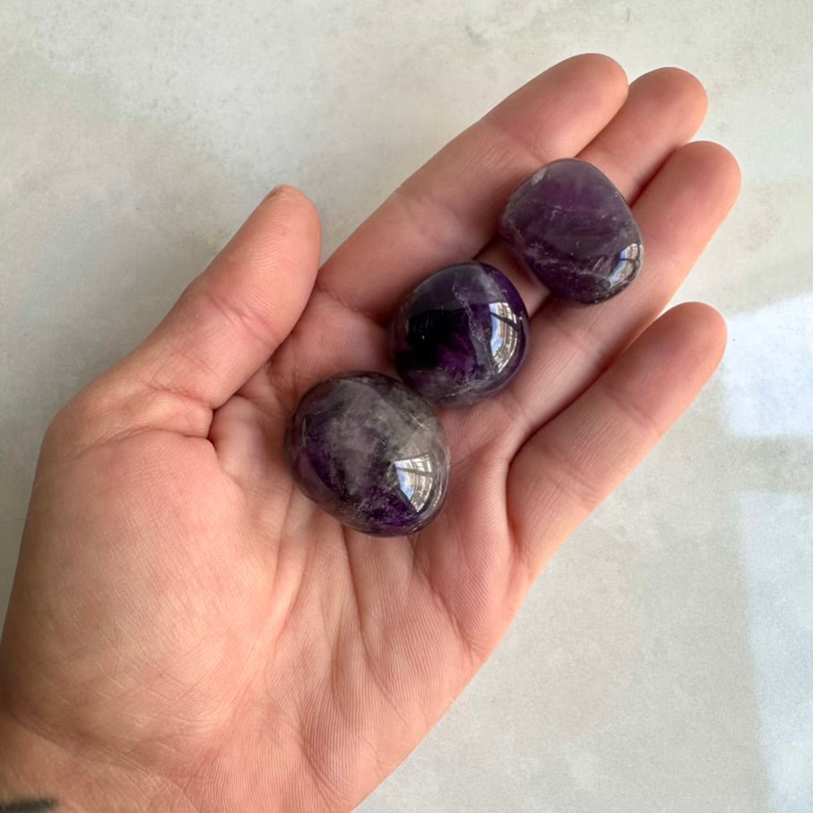 Hand holding three purple amethyst stones against a light background