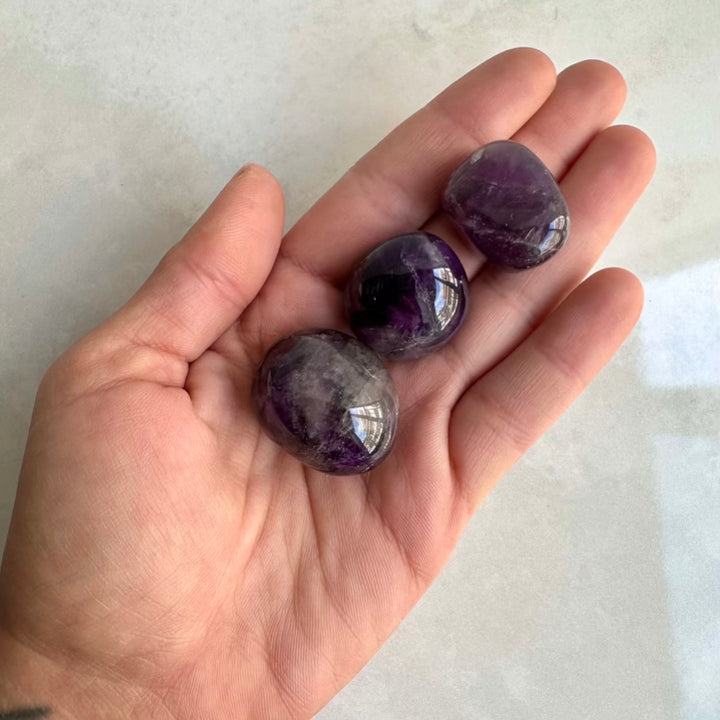 Hand holding three purple amethyst stones against a light background