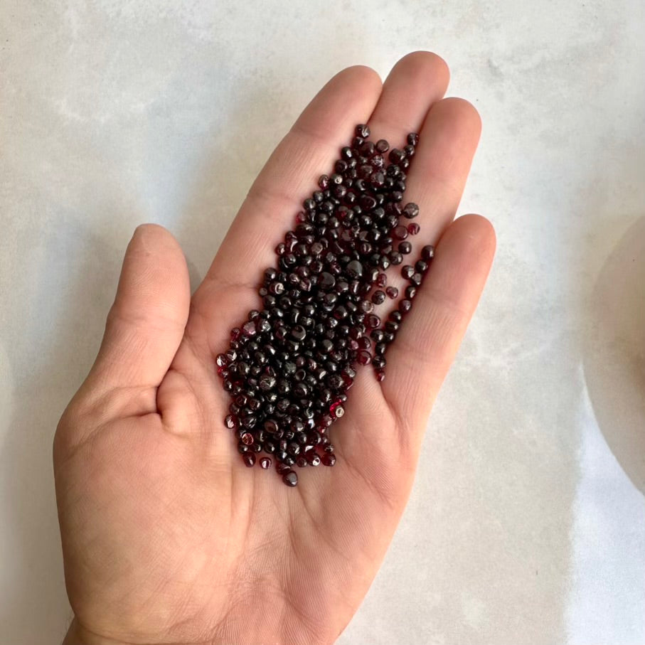 Hand holding a small pile of red garnet gemstones on a light background