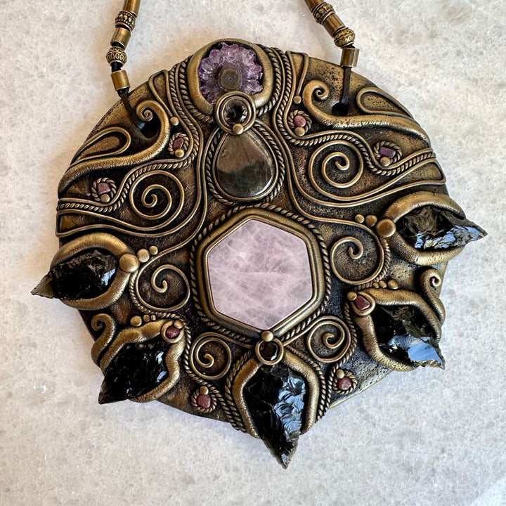 Decorative pendant with intricate designs and gemstones on a light background