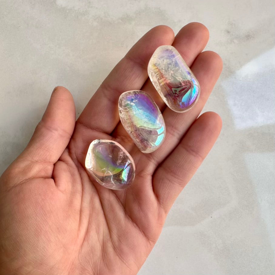 Iridescent angel aura quartz crystal stones held in a hand against a neutral background