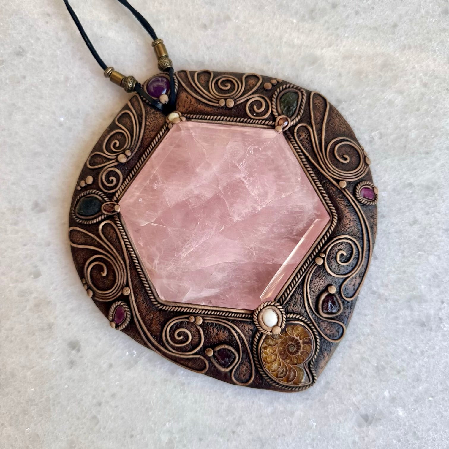 Decorative pendant with pink stone and intricate bronze frame on a light gray background