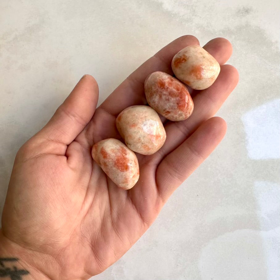 Hand holding four small, round Sunstone healing crystals for joy and confidence