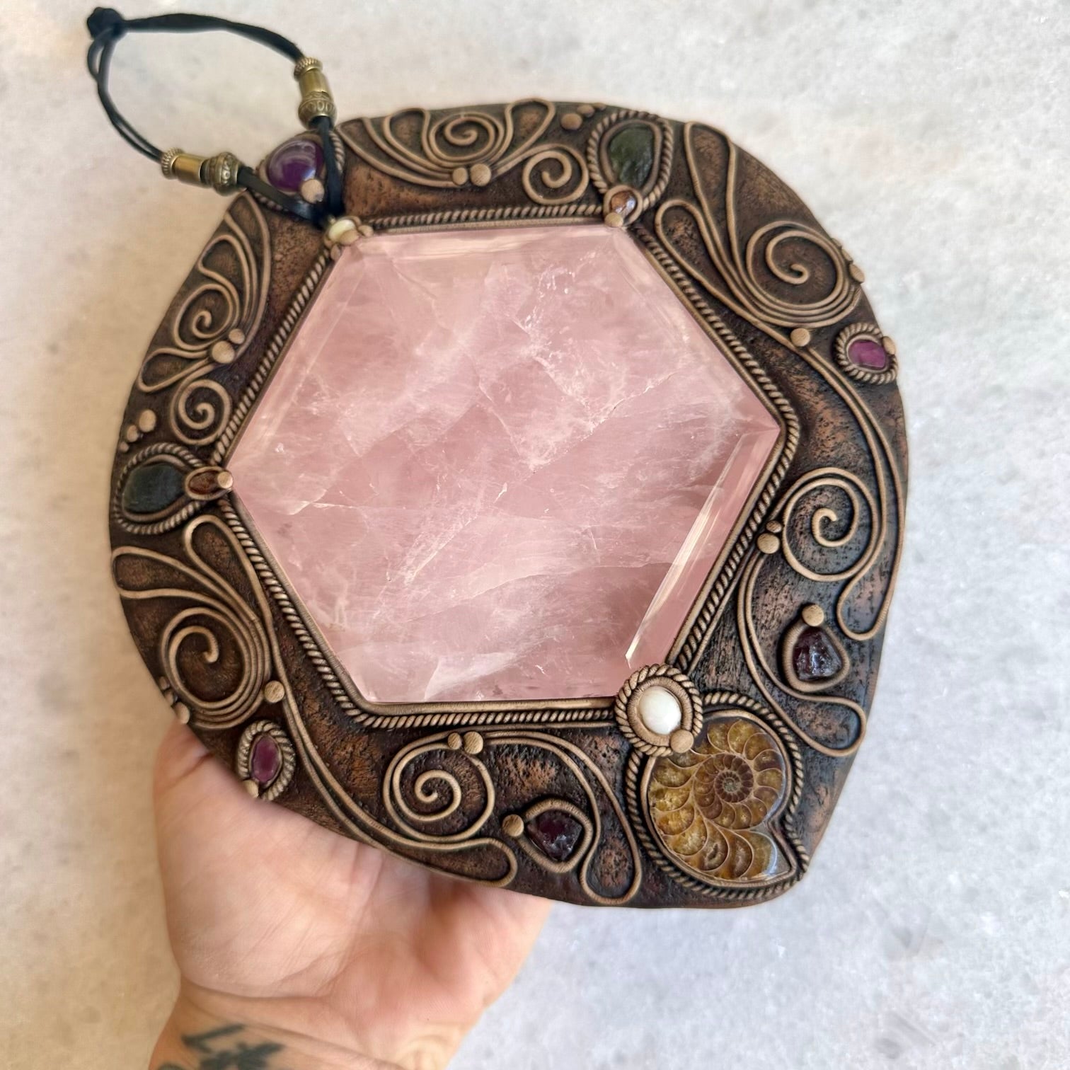 Decorative crystal with ornate bronze frame held by a hand on a light background