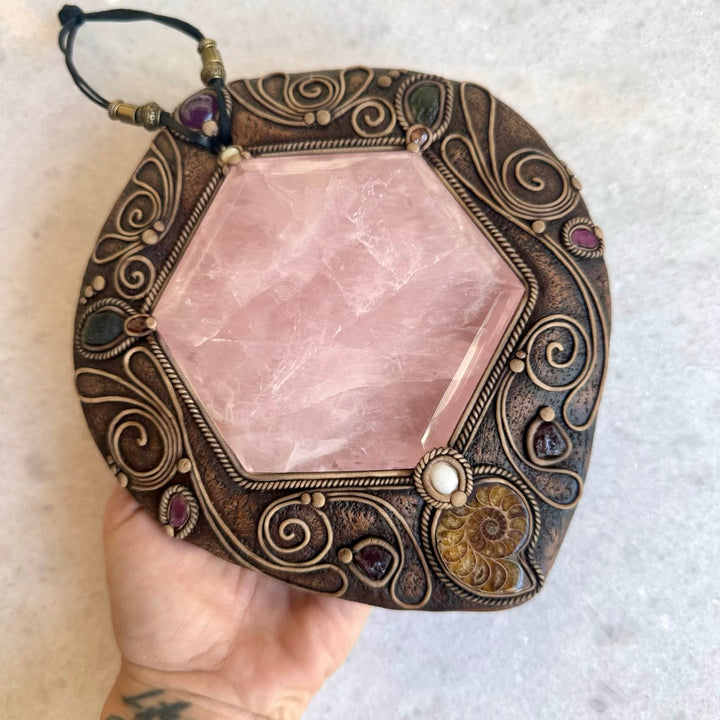 Decorative crystal with ornate bronze frame held by a hand on a light background