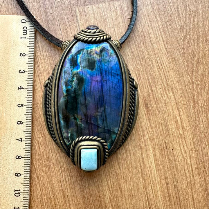 Necklace with a large, multicolored stone pendant on a wooden surface next to a ruler.