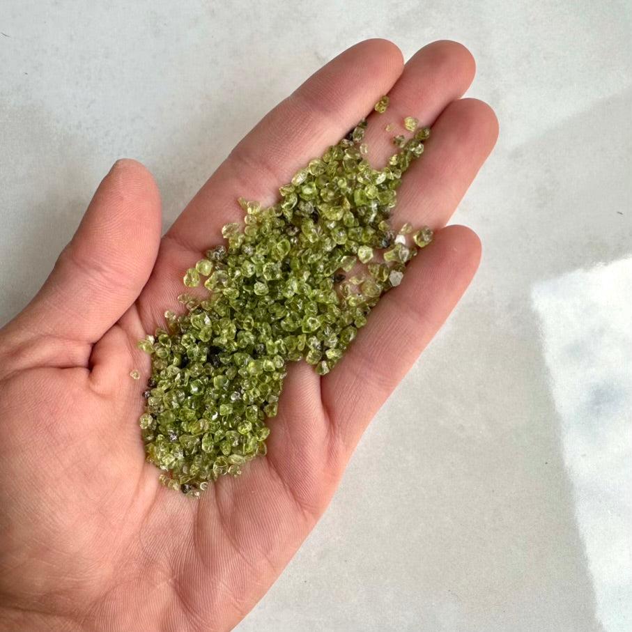 Hand holding green Natural Peridot gemstones against a light background
