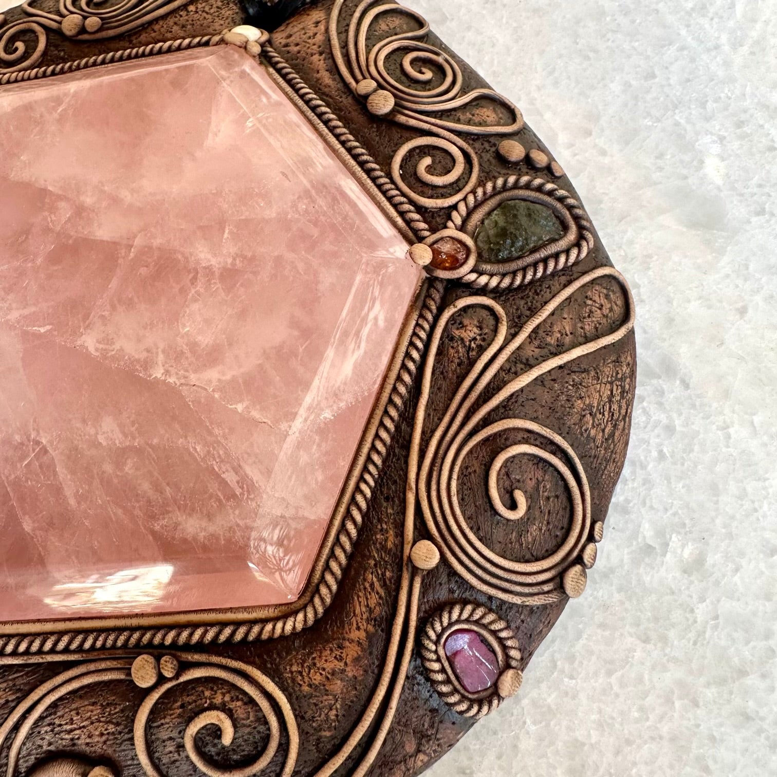 Decorative stone with rose quartz center and bronze frame on a white background