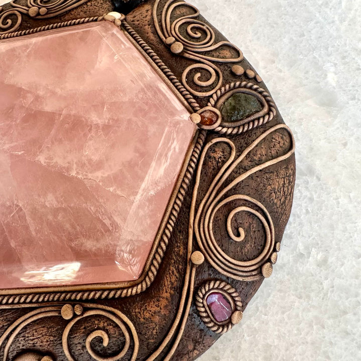 Decorative stone with rose quartz center and bronze frame on a white background