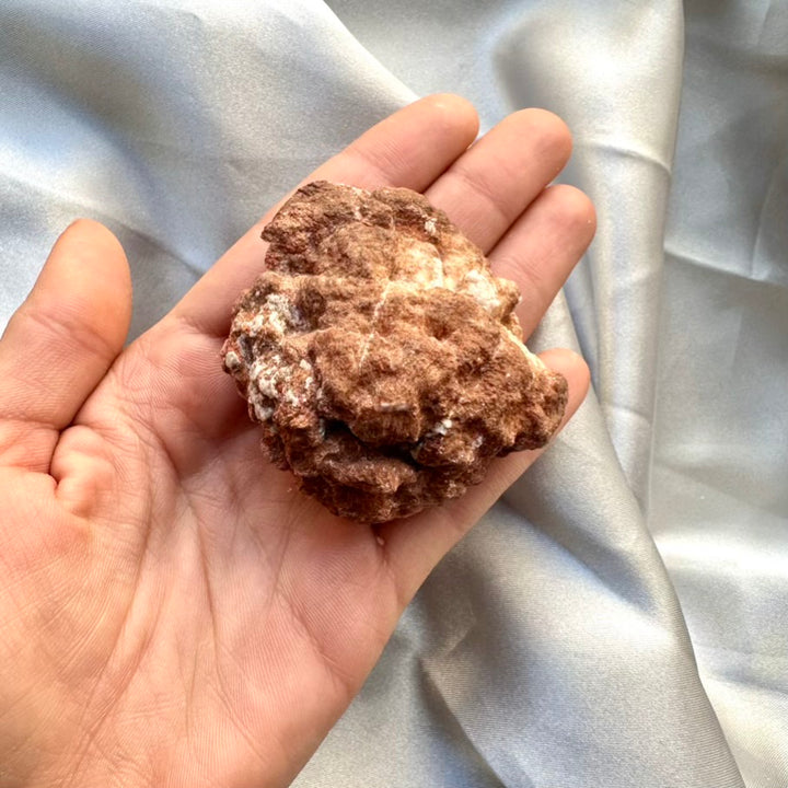 Hand holding a rough-textured brown rock against a light fabric background