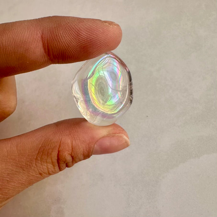 Hand holding a clear, faceted angel aura crystal against a neutral background