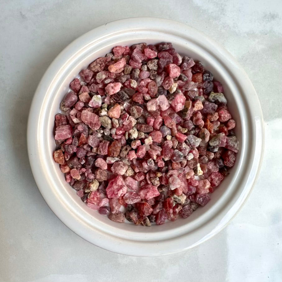 Pink spinel stone chips in a white bowl on a light gray background