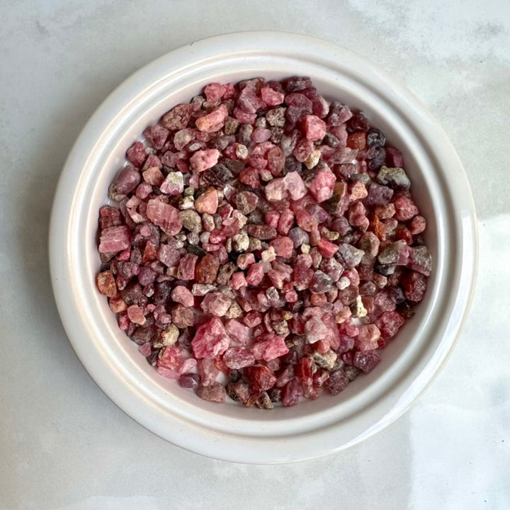 Pink spinel stone chips in a white bowl on a light gray background