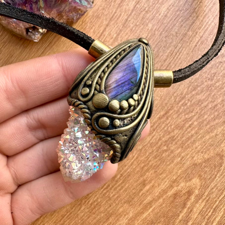Necklace with purple labradorite and aura quartz crystal held by a hand on a wooden surface