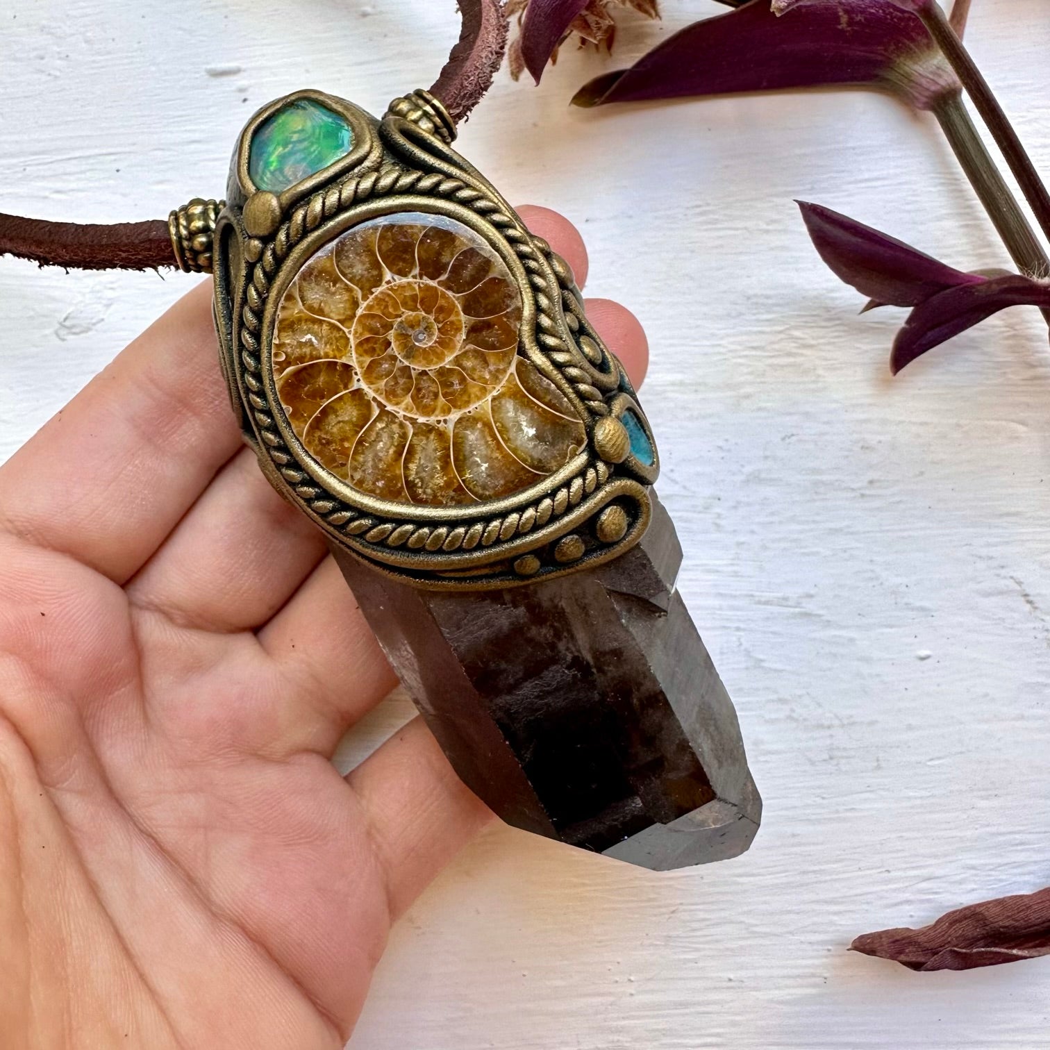 Ammonite fossil pendant on a crystal base held by a hand with a white background