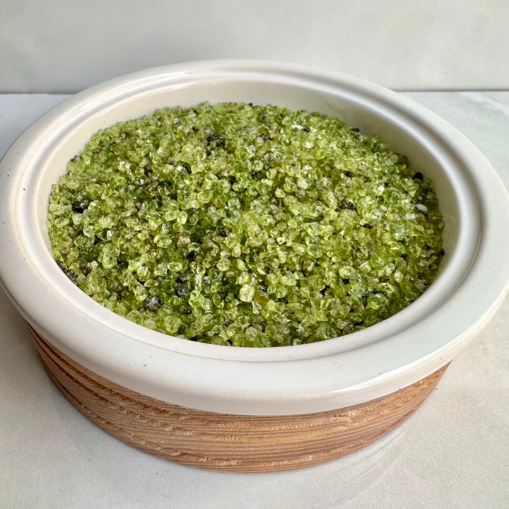 Natural Polished Peridot Gemstones in a white ceramic container on a light background
