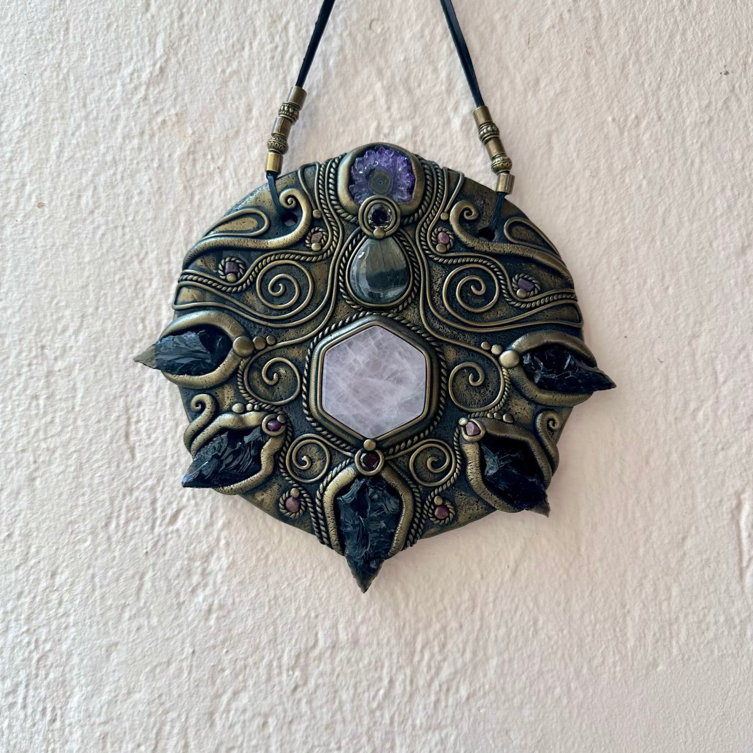 Decorative wall hanging with intricate design and stones on a white wall